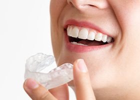 Nose-to-chin closeup of someone holding clear nightguard close to their smile