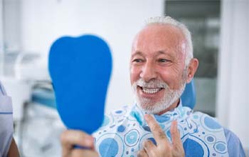 senior man admiring his new smile with dentures in Rochester