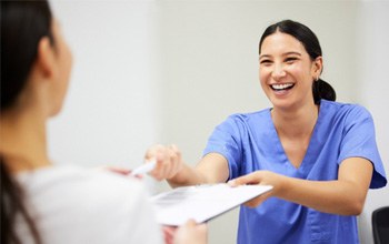 Dental assistant smiling while handing patient form