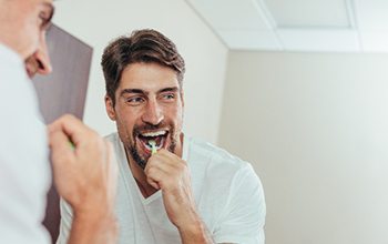 Man smiling while brushing his teeth in bathroom at home