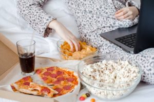 person snacking in their bed and watching movies on their laptop