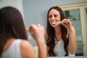 a young woman with dark hair standing in front of the bathroom mirror brushing her teeth